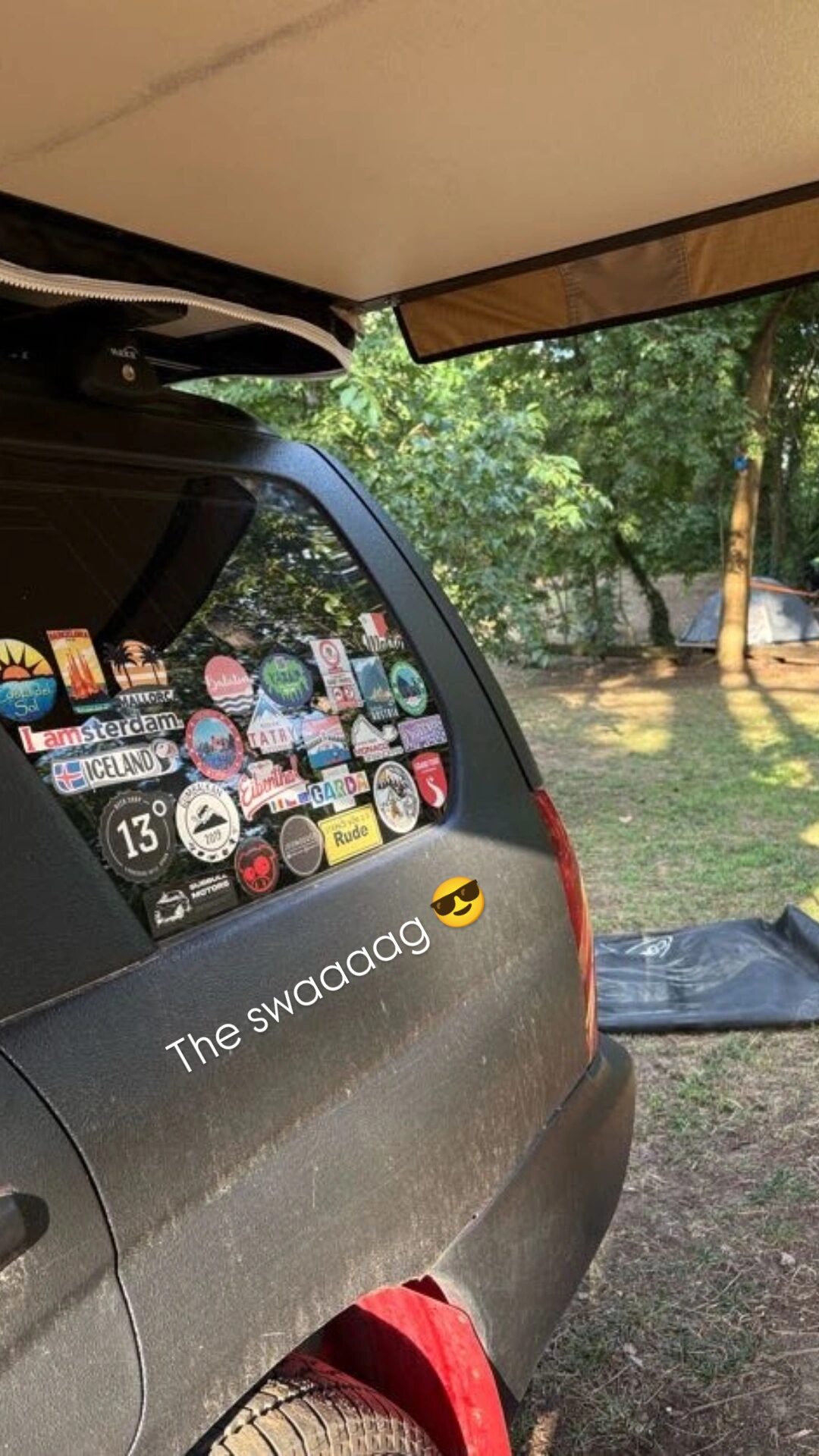 Overlander's rear window covered in travel stickers with tent visible in the forest campsite at Šumski Mir