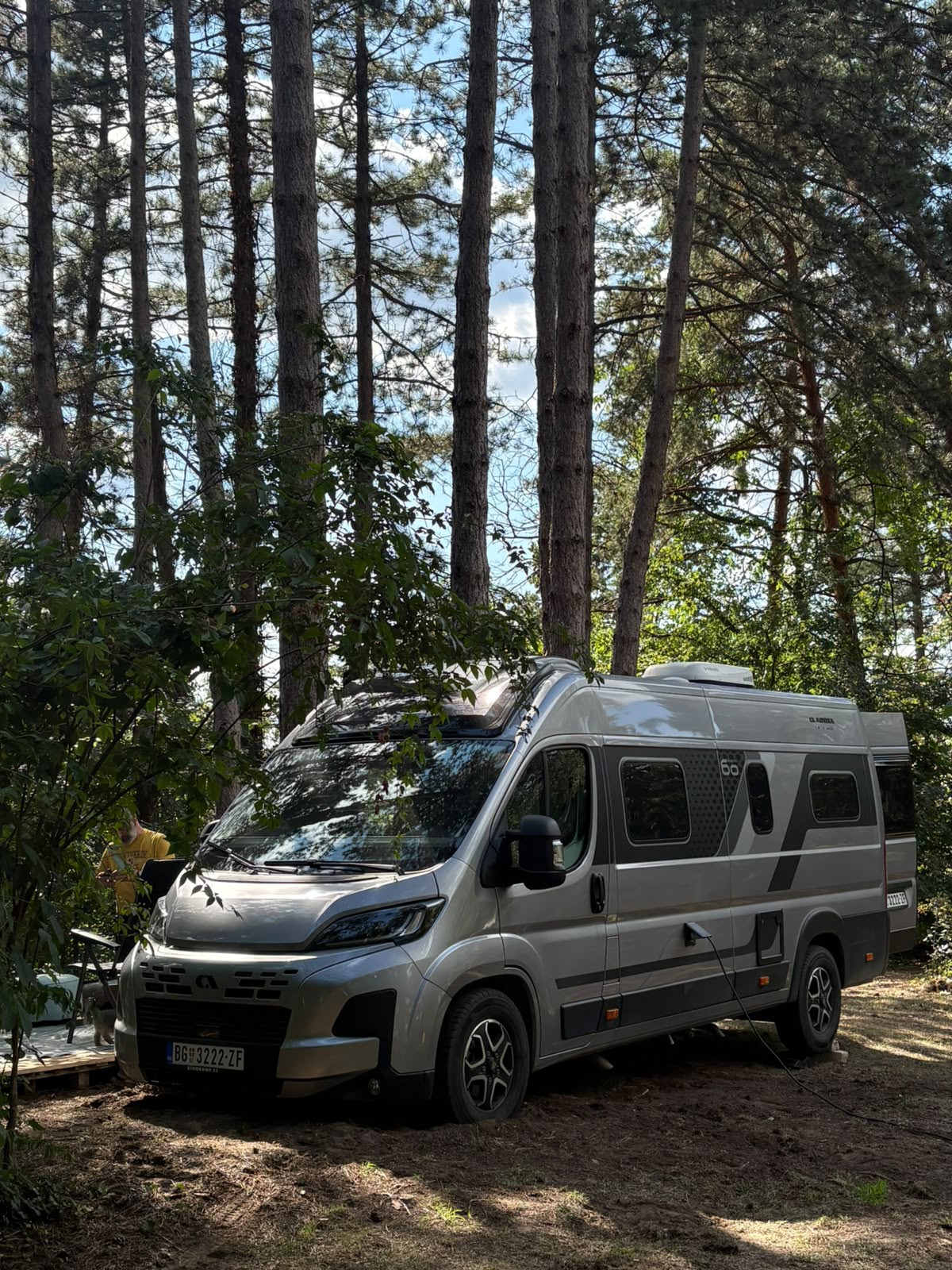 Modern camper van parked among tall pine trees at Šumski Mir campsite